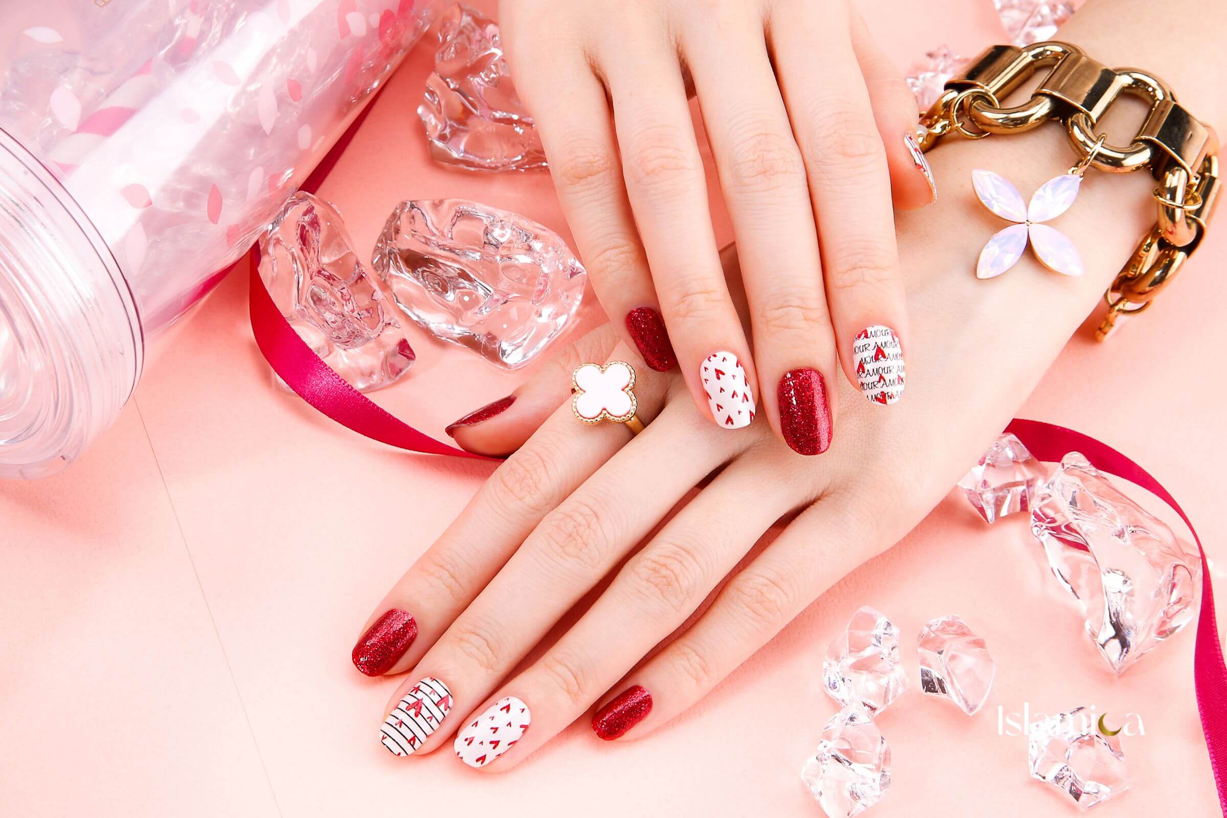 Hand met rode en witte halal nagellak, inclusief glinsterende rode tinten en speelse patronen, gestyled met gouden sieraden. Luxe en elegante nail art.
